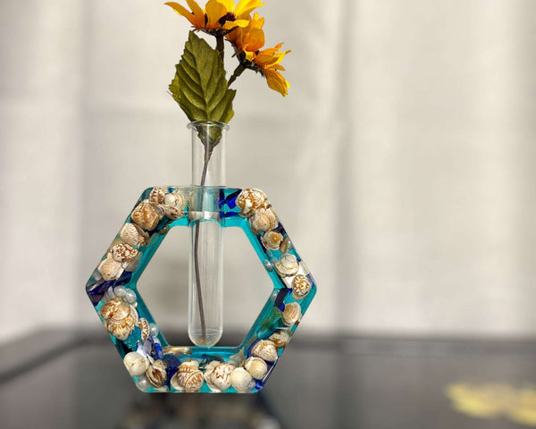 A hexagon shaped propergation bud vase created with Epoxy Resin. The first layer is filled with real seashells, the background layer is a bright teal blue. Comes with a test tube that will hold your favourite flower or plant you wish to start and root