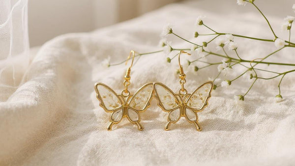 Gold butterfly earrings on a soft white surface with a blurred background