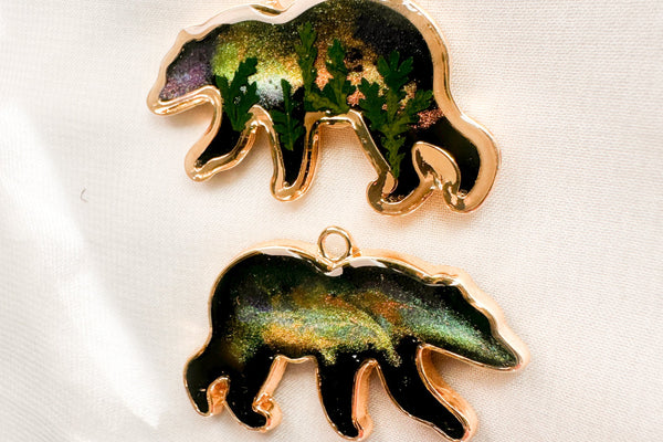 Two bear-shaped keychain with gold outlines on a white background