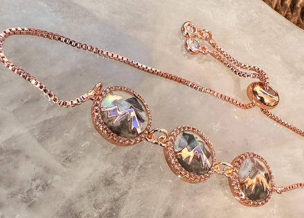 Rose gold bracelet with mother of pearl and gemstone pendants on a marble surface