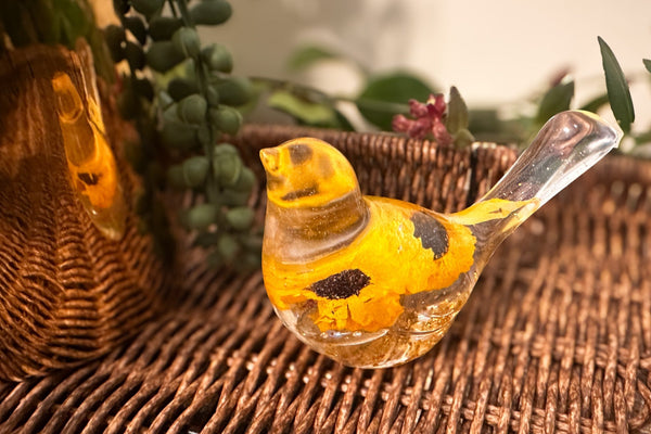 Decorative glass bottle with yellow bird design on a woven surface