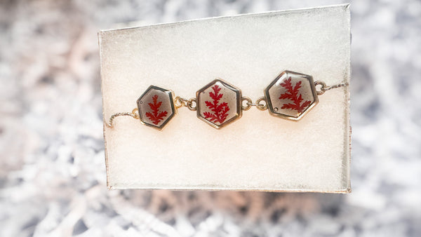 Bracelet with red floral designs on a white card against a blurred natural background