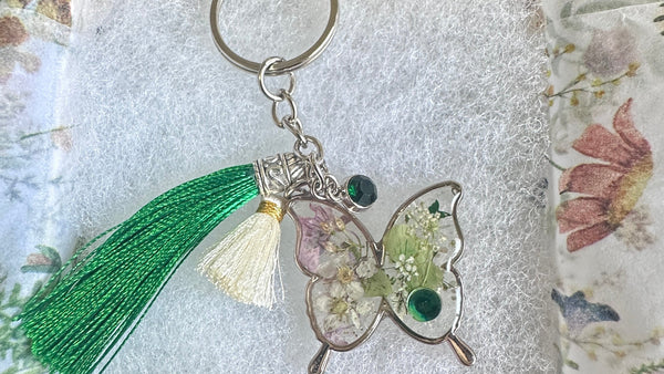 Butterfly keychain with green tassel on a floral-patterned fabric background
