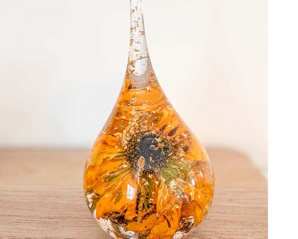 A teardrop-shaped resin ring holder containing a real Black-Eyed Susan and sunflower with gold leaf accents on a wooden surface.
