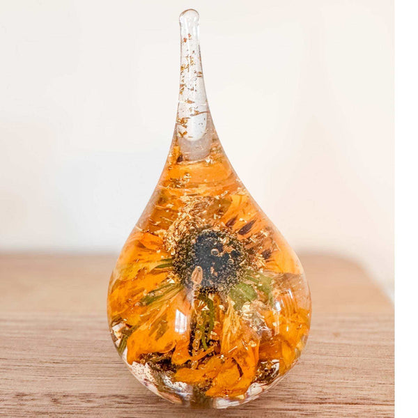 A teardrop-shaped resin ring holder containing a real Black-Eyed Susan and sunflower with gold leaf accents on a wooden surface.