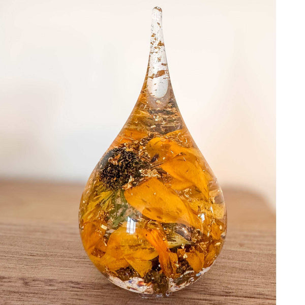 A teardrop-shaped resin ring holder containing a real Black-Eyed Susan and sunflower with gold leaf accents on a wooden surface.