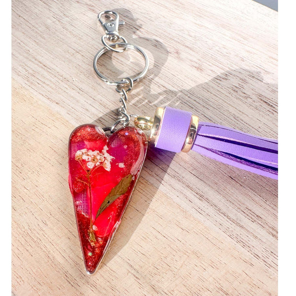 Antique silver heart bag charm filled with pink and purple resin and real white flowers, attached to a purple leather tassel