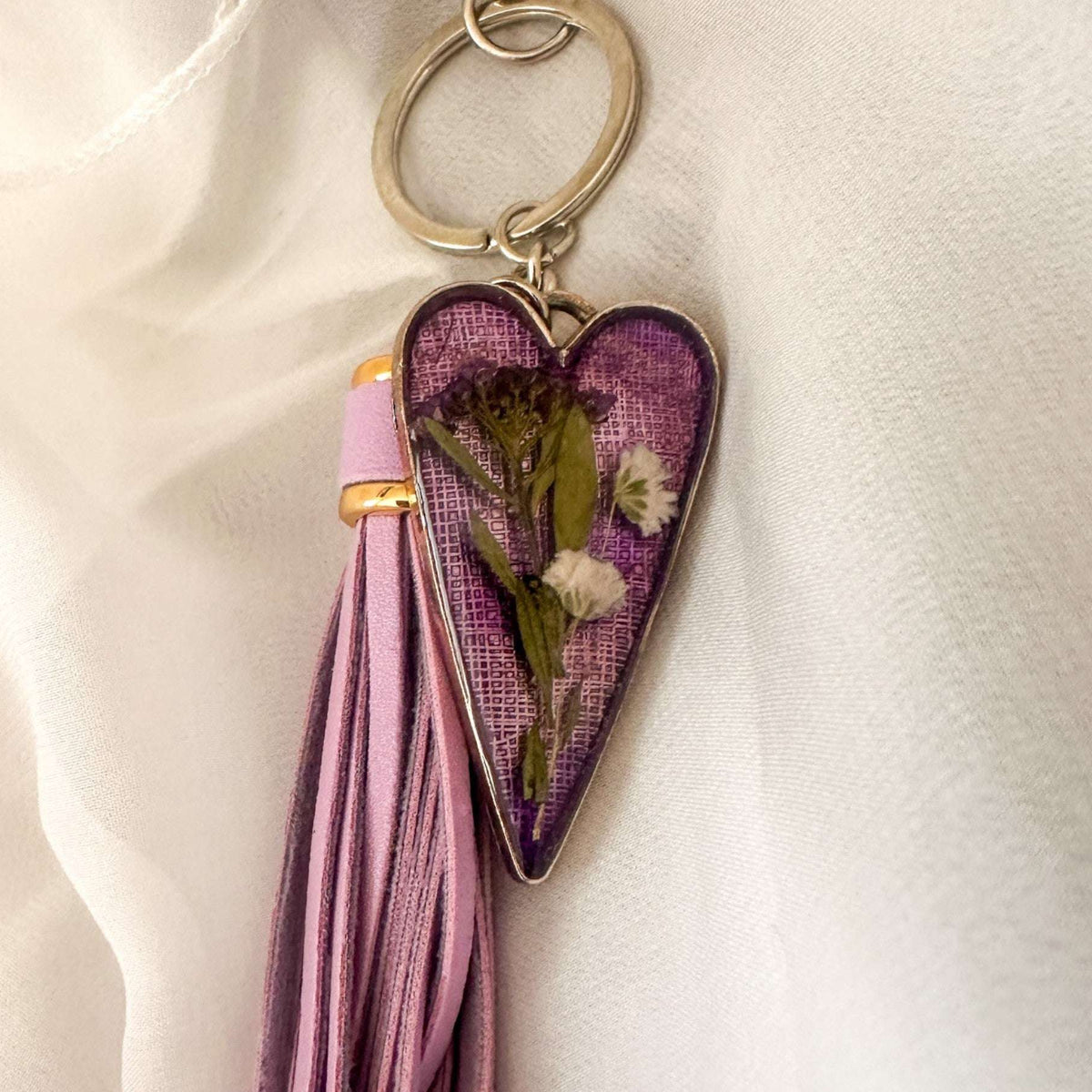 Antique silver Lavender Skies heart bag charm with a soft purple resin background and white dried flowers, attached to a matching purple leather tassel.