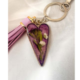  Antique silver Lavender Skies heart bag charm with a soft purple resin background and white dried flowers, attached to a matching purple leather tassel. with dried flowers on a white background