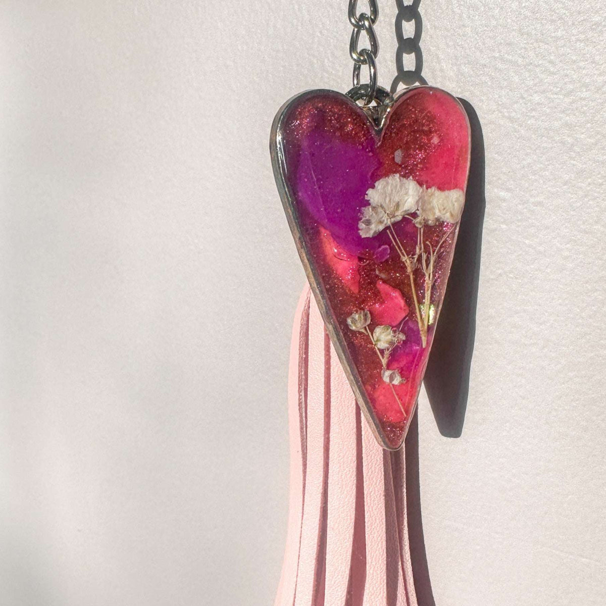 Close up of real white pressed flowers encased in vibrant pink and purple tinted resin inside a silver heart frame.
