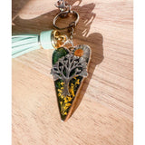 Secret Garden Bag Charm & Silver Tree of Life heart charm with a moss green resin background, real yellow flowers, and a tiny daisy, featuring a green leather tassel.