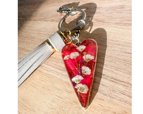 Antique silver heart bag charm filled with pink and purple resin and real white flowers, attached to a gray leather tassel