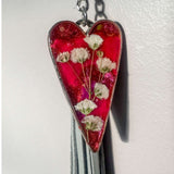 Close up of real white pressed flowers encased in vibrant pink and purple tinted resin inside a silver heart frame.