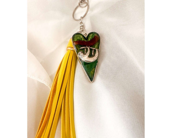 Close up of the silver sloth heart bag charm and real preserved greenery encased in shimmering green resin.