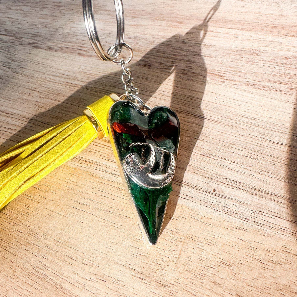 Close up of the silver sloth heart bag charm and real preserved greenery encased in shimmering green resin.