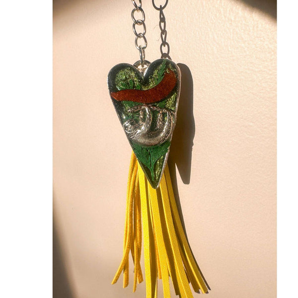 Close up of the silver sloth heart bag charm and real preserved greenery encased in shimmering green resin.