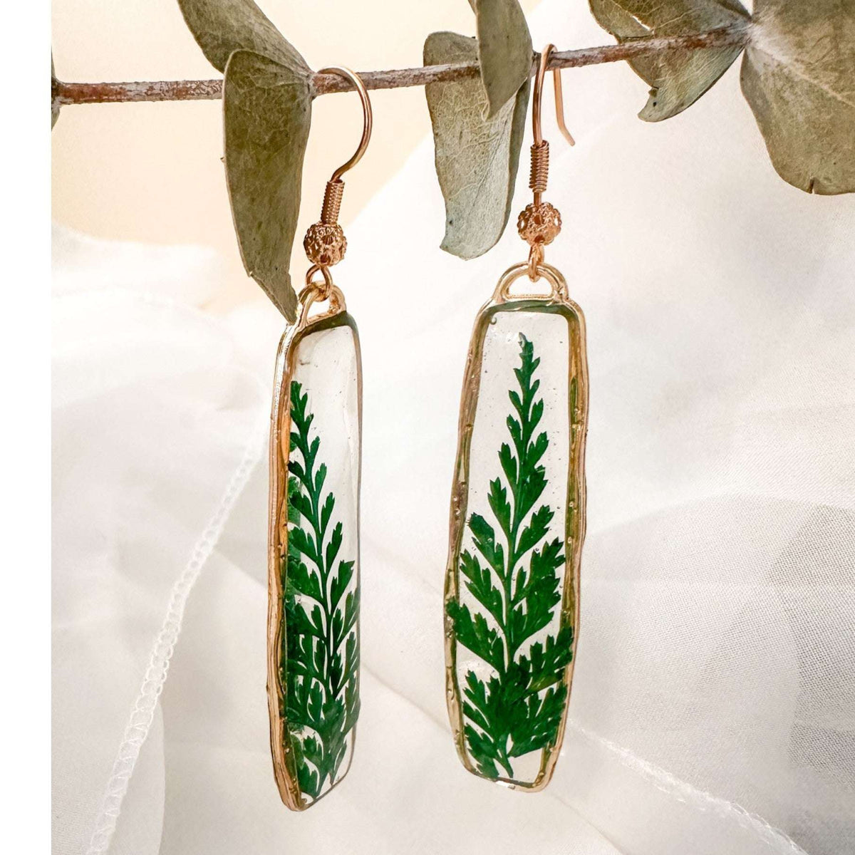 Close-up of the natural sculpted edges of these minimalist boho fern drop earrings in gold.