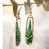 Close-up of the natural sculpted edges of these minimalist boho fern drop earrings in gold.