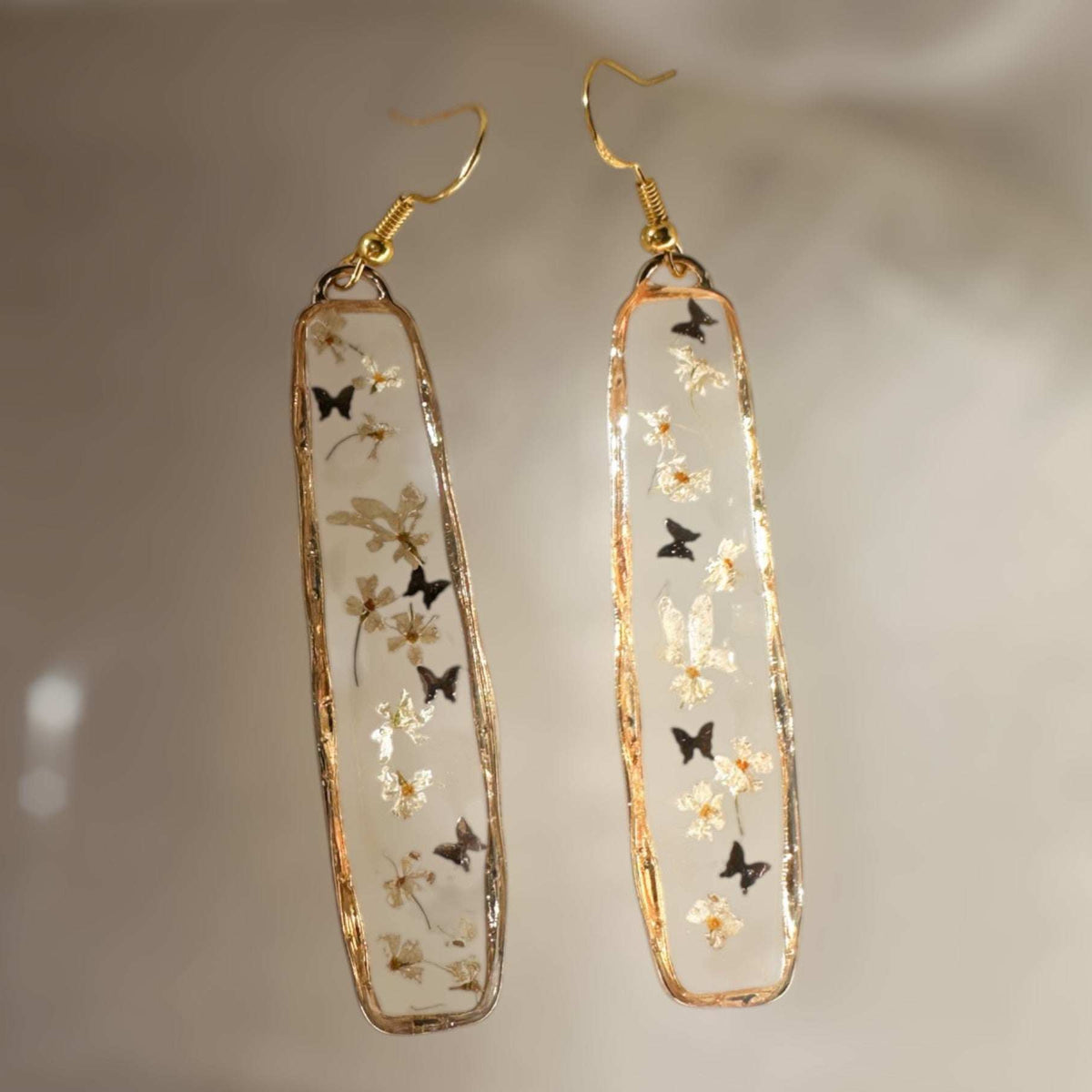 Long organic-edged Floral Butterfly drop earrings featuring tiny white spring flowers and miniature butterflies floating in clear resin.