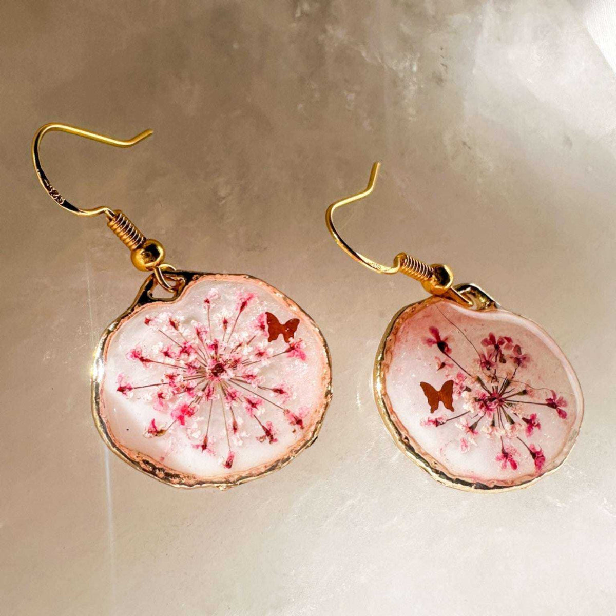 Close up of dark pink Queen Anne's Lace and a tiny floating butterfly inside pink floral butterfly earrings.