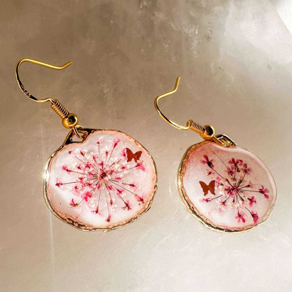 Close up of dark pink Queen Anne's Lace and a tiny floating butterfly inside pink floral butterfly earrings.
