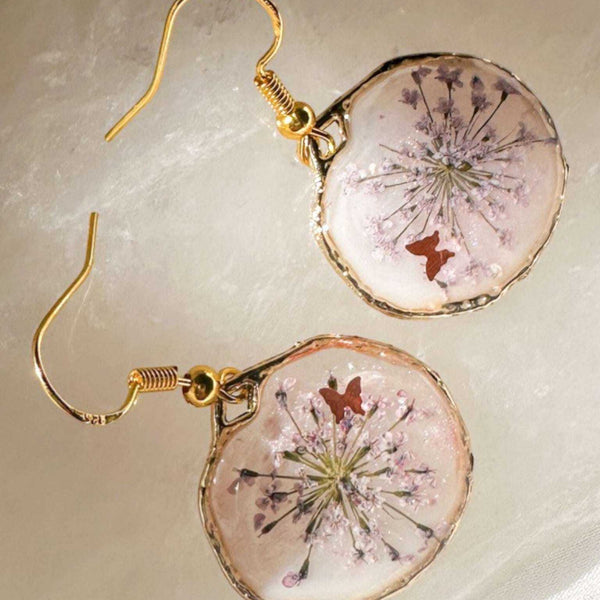 Close up of dark pink Queen Anne's Lace and a tiny floating butterfly inside pink floral butterfly earrings.