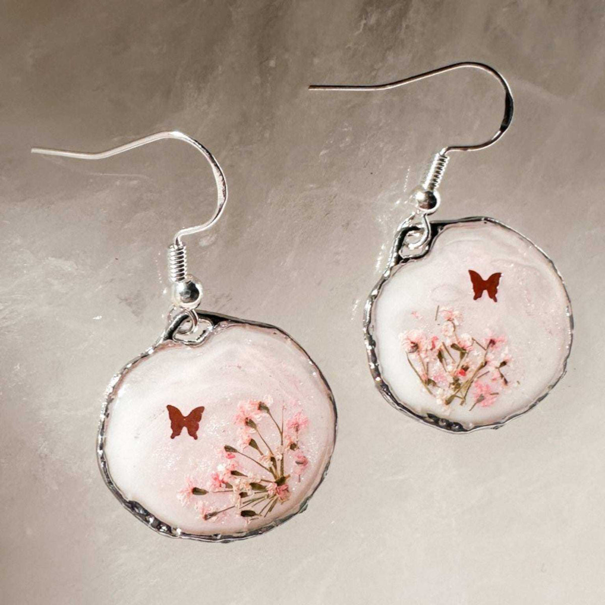 Close up of dark pink Queen Anne's Lace and a tiny floating butterfly inside pink floral butterfly earrings.
