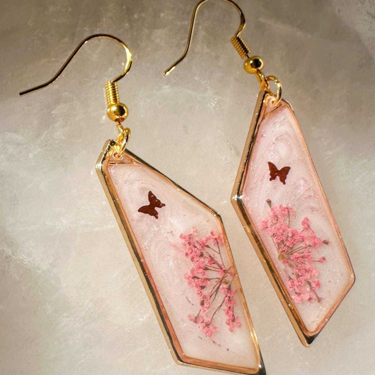 Close up of pressed pink butterfly resin earrings with Queen Anne's Lace and a floating butterfly charm in clear resin.