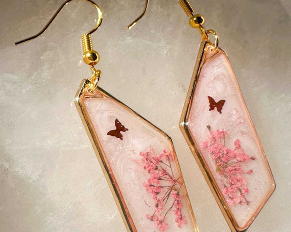 Close up of pressed pink butterfly resin earrings with Queen Anne's Lace and a floating butterfly charm in clear resin.