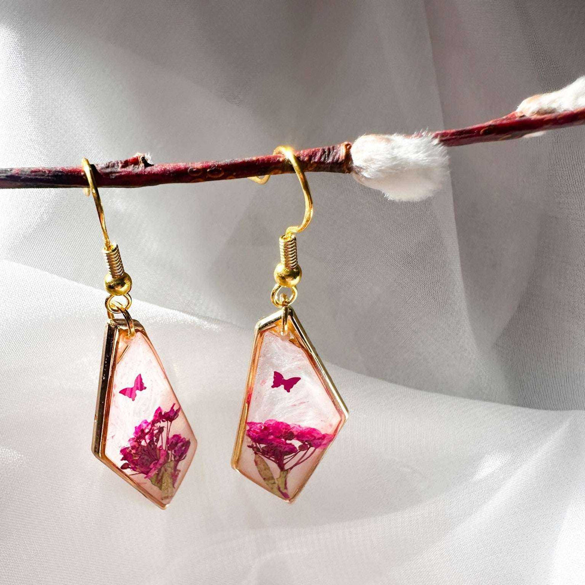 Whimsical pink floral butterfly earrings styled on a white crystal background, handmade pink butterfly resin earrings
