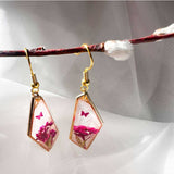 Whimsical pink floral butterfly earrings styled on a white crystal background, handmade pink butterfly resin earrings