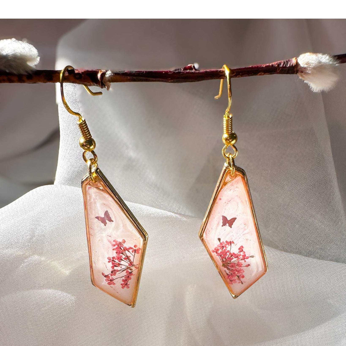 Whimsical pink butterfly resin earrings with butterfly styled on a white crystal background.