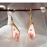 Whimsical pink butterfly resin earrings with butterfly styled on a white crystal background.