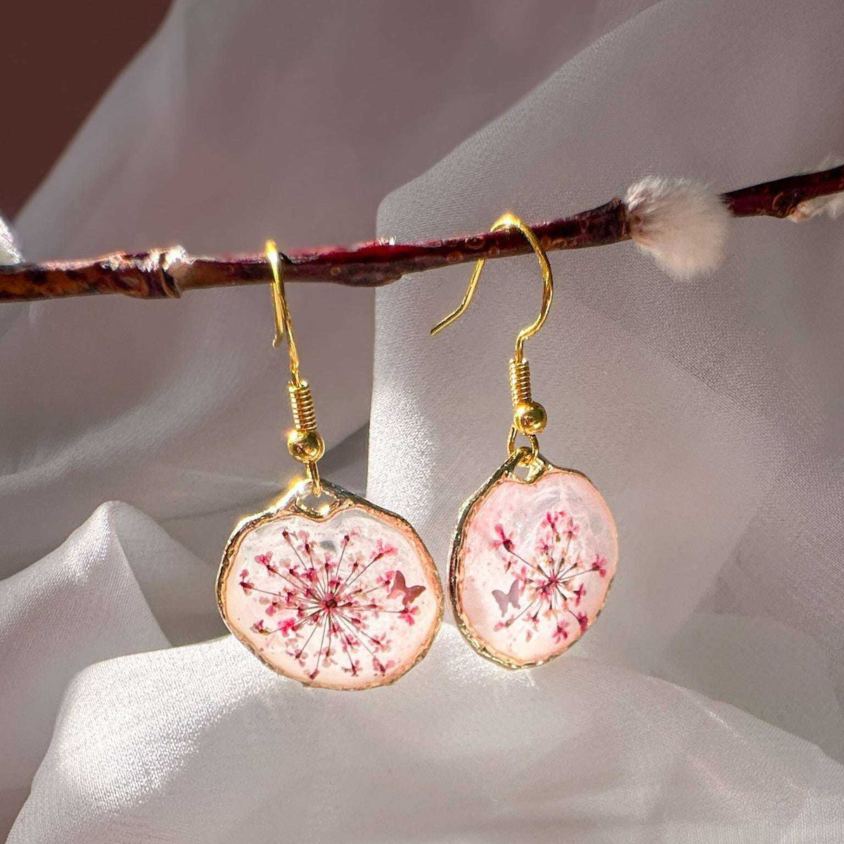 Close up of dark pink Queen Anne's Lace and a tiny floating butterfly inside pink floral butterfly earrings.
