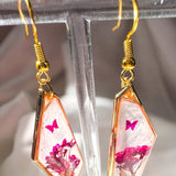 Whimsical pink butterfly resin earrings with butterfly styled on a white crystal background.
