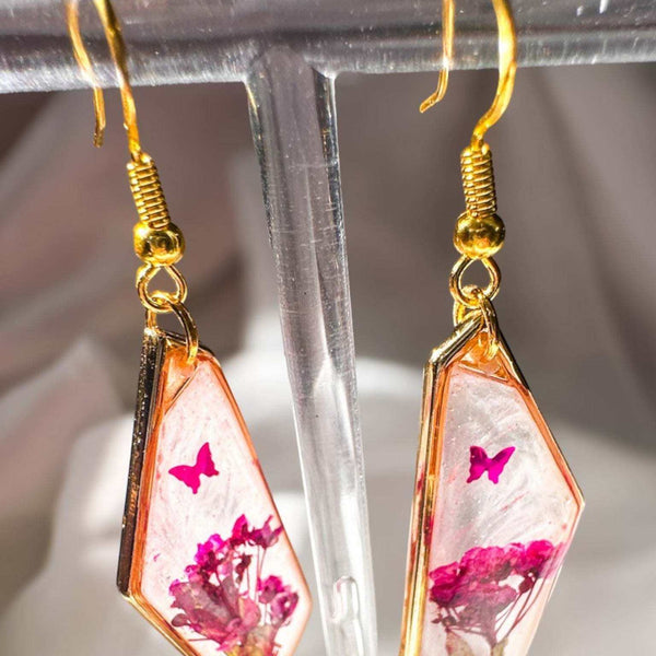 Whimsical pink butterfly resin earrings with butterfly styled on a white crystal background.