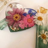 Close-up of real pink daisies and white floral accents inside a clear resin heart.