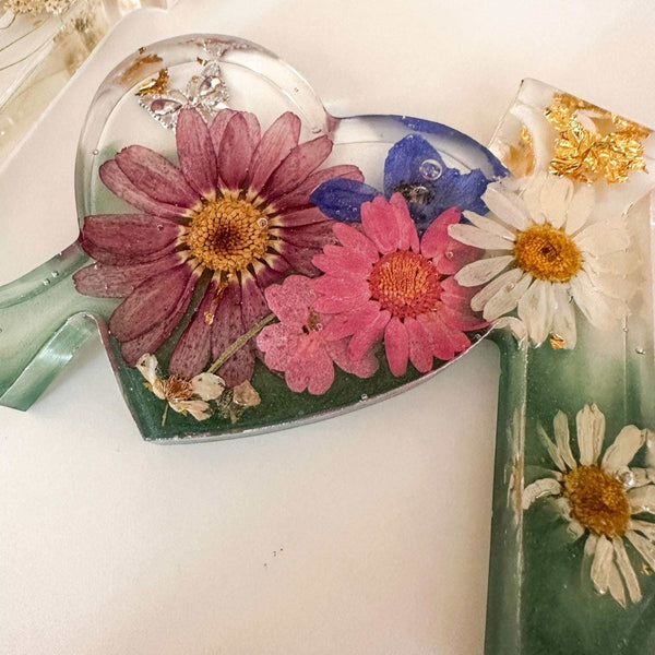 Close-up of real pink daisies and white floral accents inside a clear resin heart.