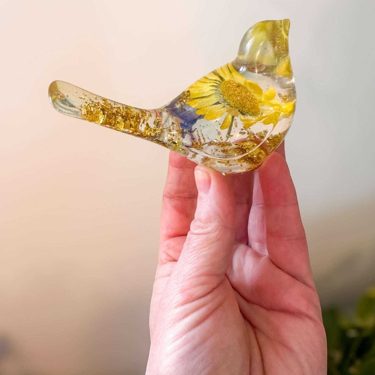 Close-up of a real yellow daisy and purple accent flowers inside a clear resin bird.