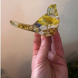 Close-up of a real yellow daisy and purple accent flowers inside a clear resin bird.