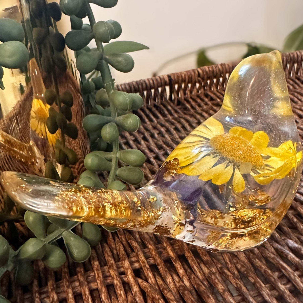Close-up of a real yellow daisy and purple accent flowers inside a clear resin bird.