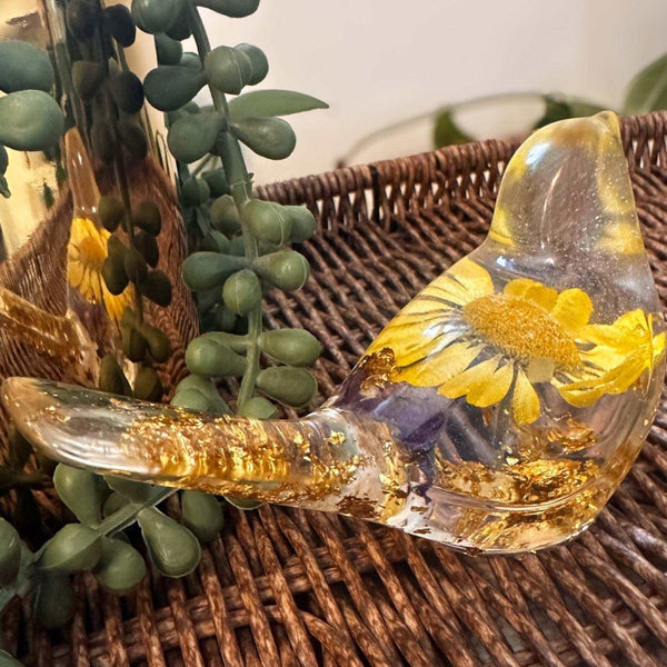 Close-up of a real yellow daisy and purple accent flowers inside a clear resin bird.
