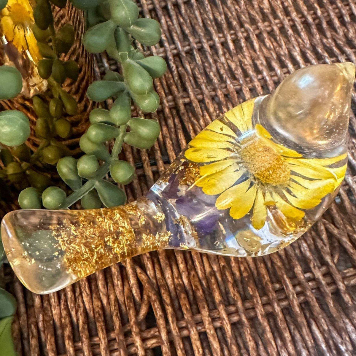 Close-up of a real yellow daisy and purple accent flowers inside a clear resin bird.