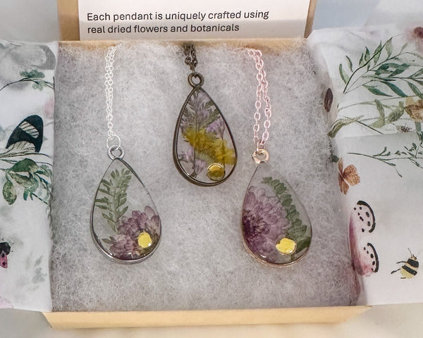 Three teardrop-shaped pendants with floral designs on a branded card with product details.