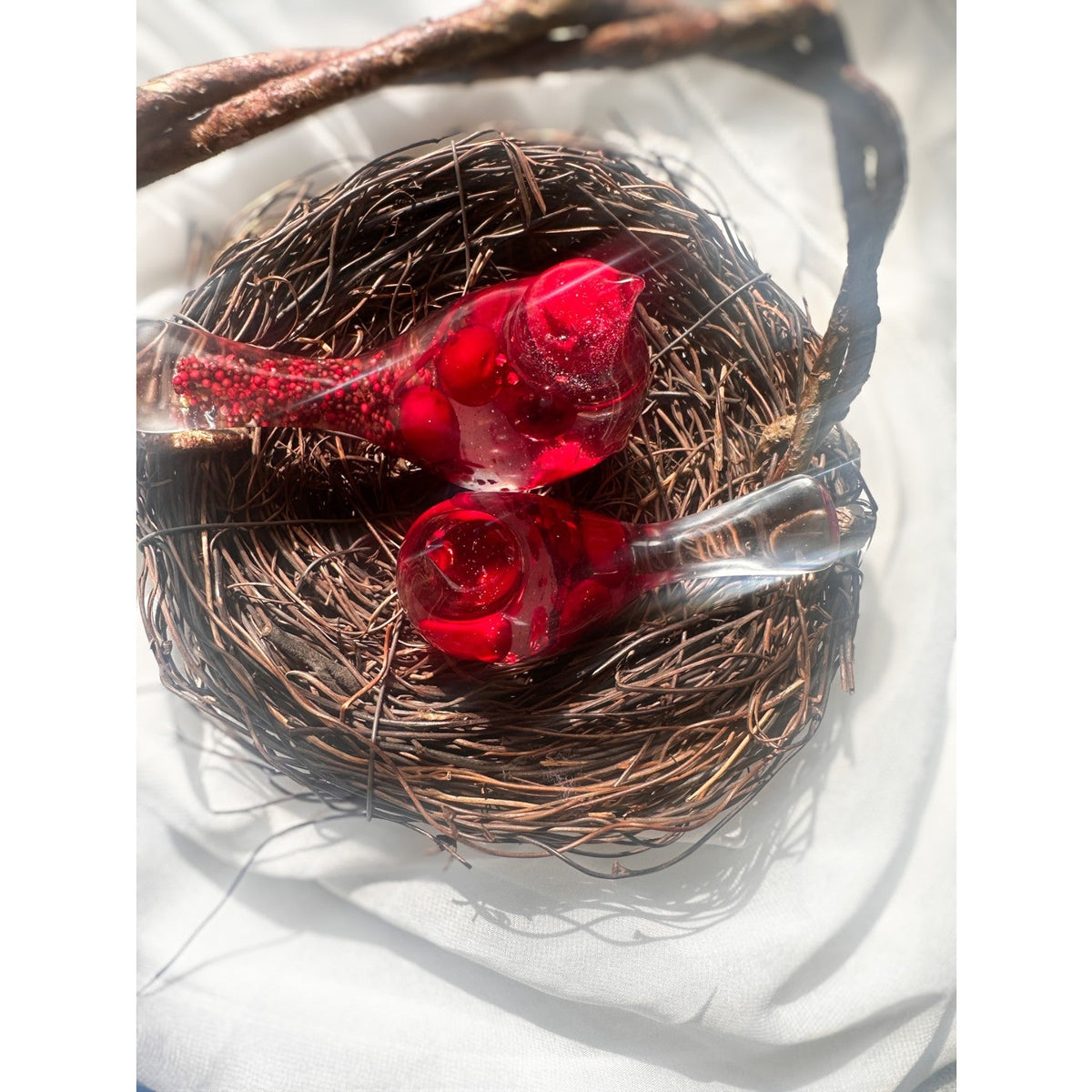 Close-up of glossy red berries suspended in clear hand-poured resin bird with red glitter shimmer in a wicker style nest
