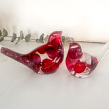 Close-up of glossy red berries suspended in clear hand-poured resin bird with red glitter shimmer