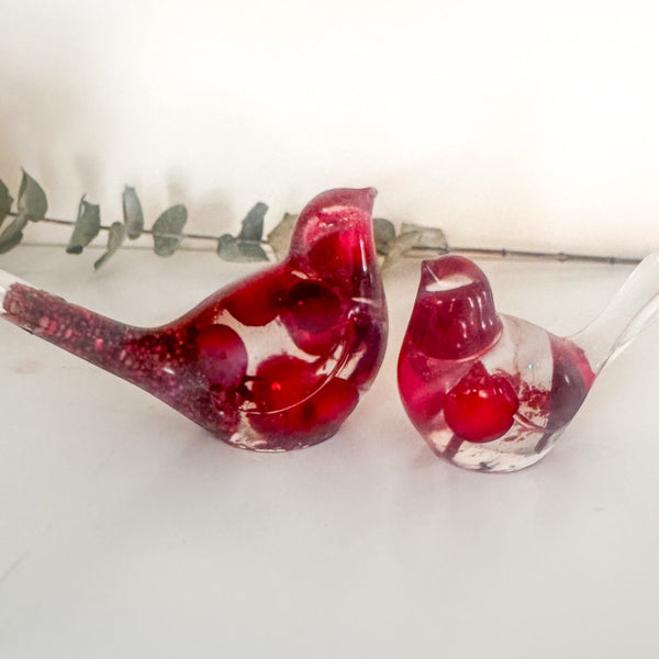 Close-up of glossy red berries suspended in clear hand-poured resin bird with red glitter shimmer