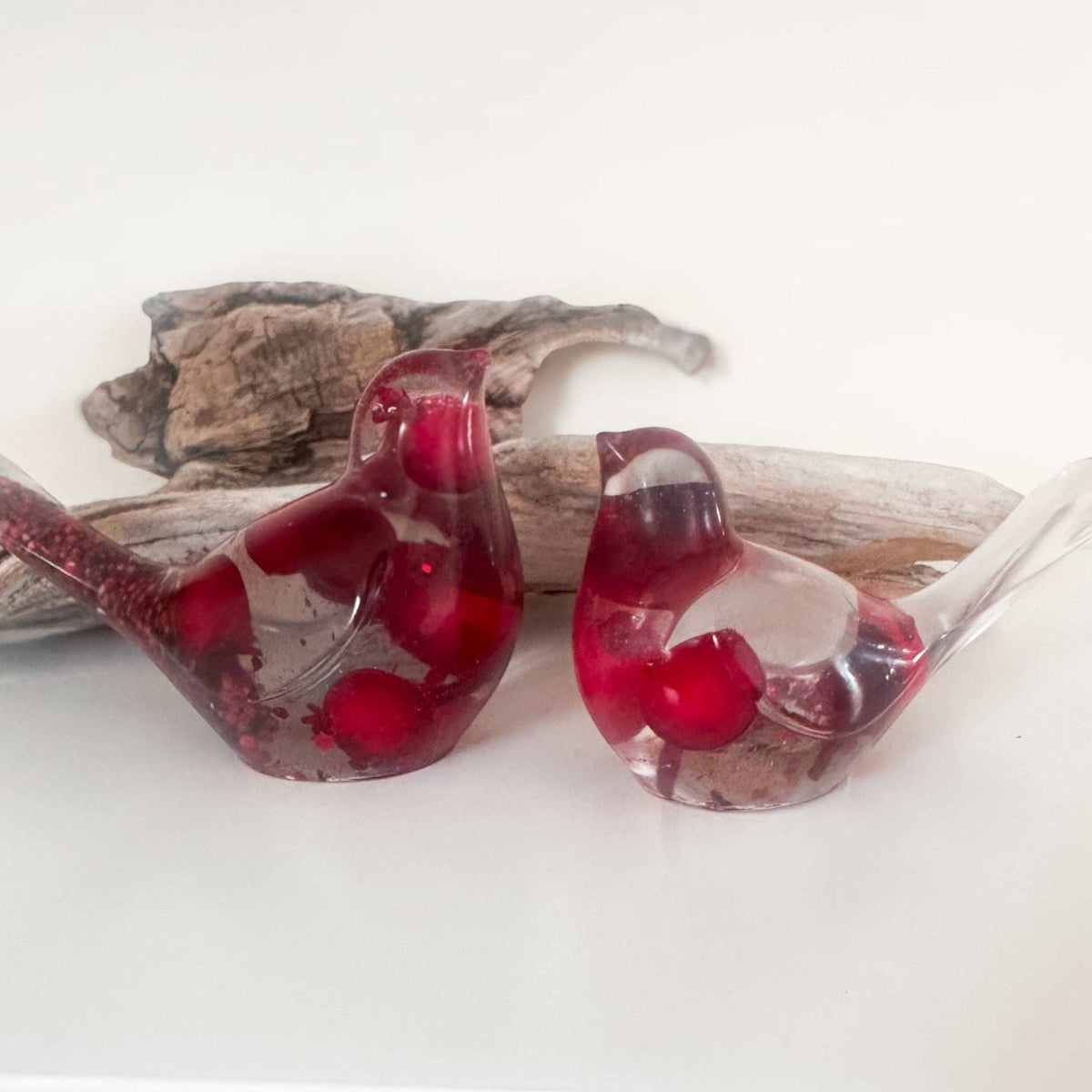 Close-up of glossy red berries suspended in clear hand-poured resin bird with red glitter shimmer