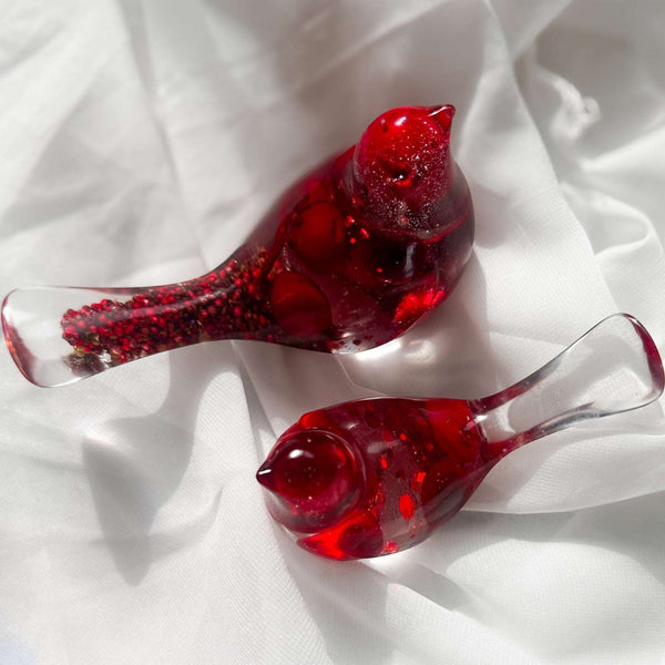 Close-up of glossy red berries suspended in clear hand-poured resin bird with red glitter shimmer