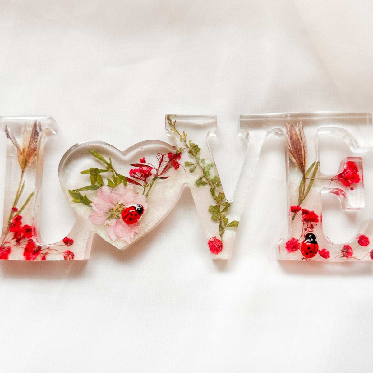 Close-up of real foraged garden greenery and red ladybug charms in resin
